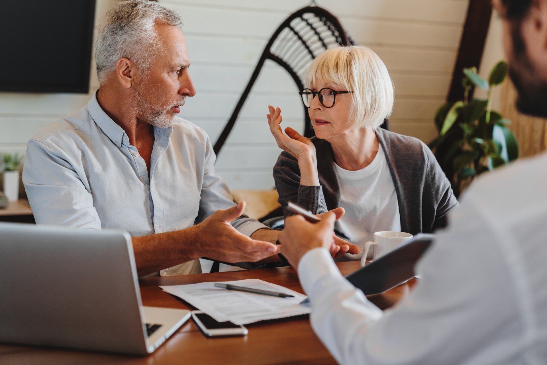 Financial advisor giving retirement advice to old couple while they arguing at home interior Financial advisor giving retirement advice to old couple while they arguing at home interior